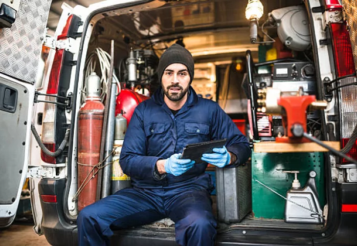 Technician in in back of work van in coveralls with ipad in hands